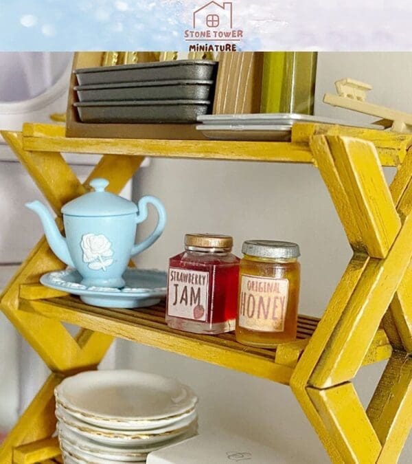 Miniature shelf with a blue teapot, strawberry jam, honey jars, and stacked plates. Cozy display scene.