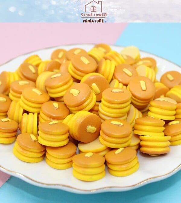 Miniature pancake stack replicas on a plate, each topped with a small butter pat.