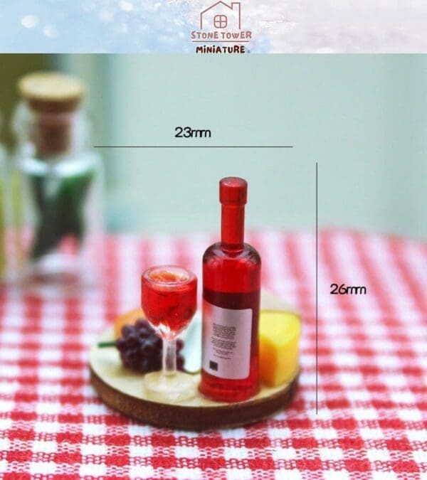 Miniature red wine bottle and glass on a checkered cloth with grapes and cheese, labeled dimensions 23mm by 26mm.