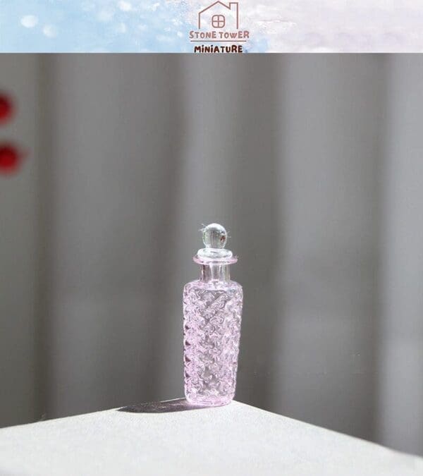 Pink glass miniature perfume bottle on a sunlit surface with a patterned design.