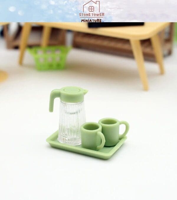 Miniature green pitcher and cups set on a tray, placed on a white surface with blurred wooden furniture in the background.