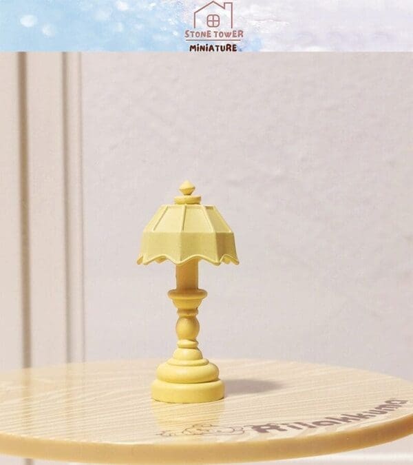 Miniature yellow lamp on a wooden table, with a scalloped shade. Background shows blurred interior wall details.