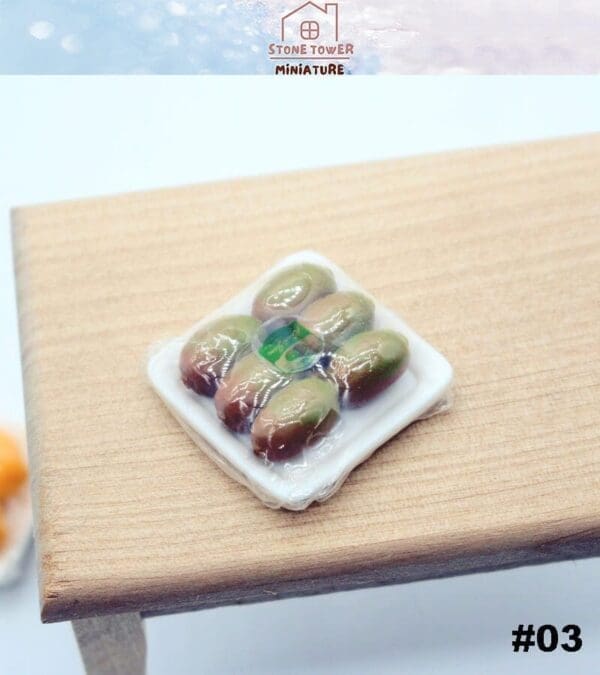 Miniature plastic-wrapped tray with small realistic olives on a wooden surface.