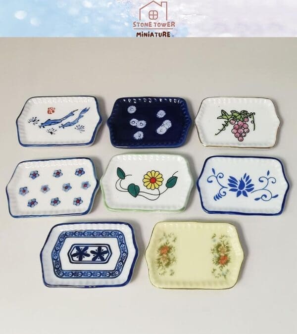 Seven rectangular miniature plates with various floral and abstract designs on a white background.