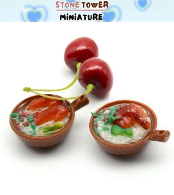 Miniature clay bowls with food and two realistic cherries, set against a backdrop with blue heart designs.