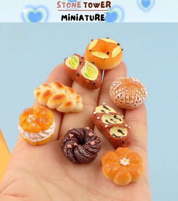 Hand holding miniature bread and pastries, intricately detailed with different shapes and toppings on a light blue background.