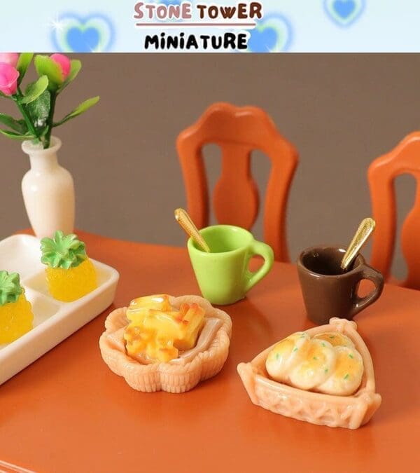 Miniature table setting with pastries, two tiny mugs, and a vase with pink flowers on an orange table.