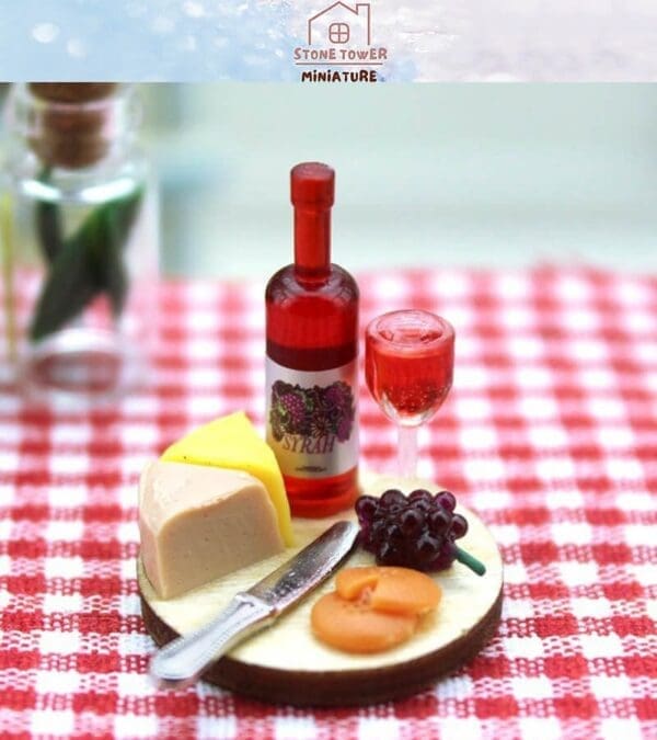 Miniature cheese, grapes, and figs with red wine bottle and glass on a checkered tablecloth.