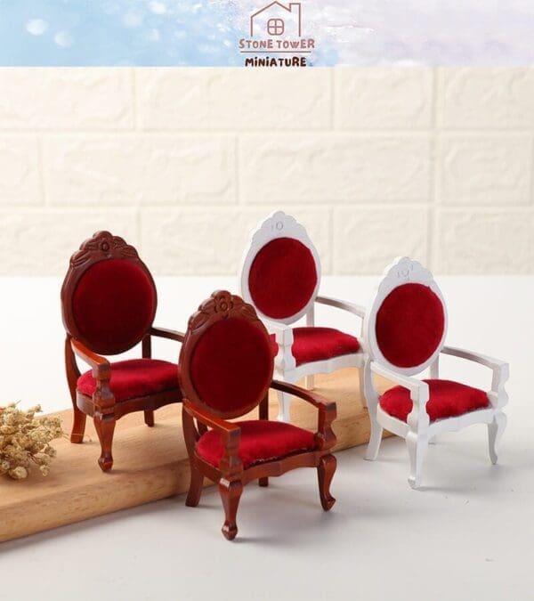 Miniature red velvet chairs with ornate designs in wood and white finishes on a wooden plank.