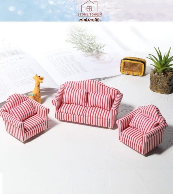 Miniature striped red and white sofa set with a book, giraffe figurine, vintage radio, and potted plant on a white surface.