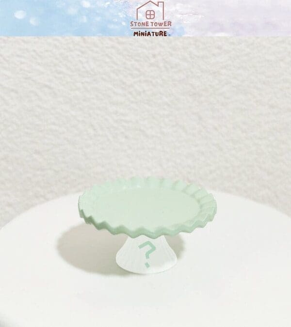 Mint green miniature cake stand on a white surface, stone texture background.