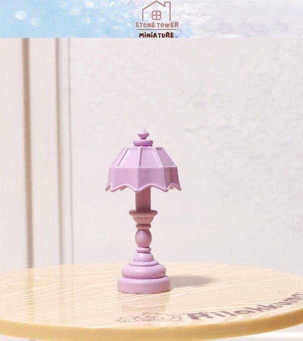 Miniature pink table lamp with a scalloped shade on a light wooden surface.