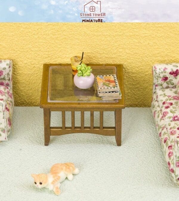 Miniature living room with wooden table, floral sofas, a book, plant, drink, and small cat figurine on the floor.