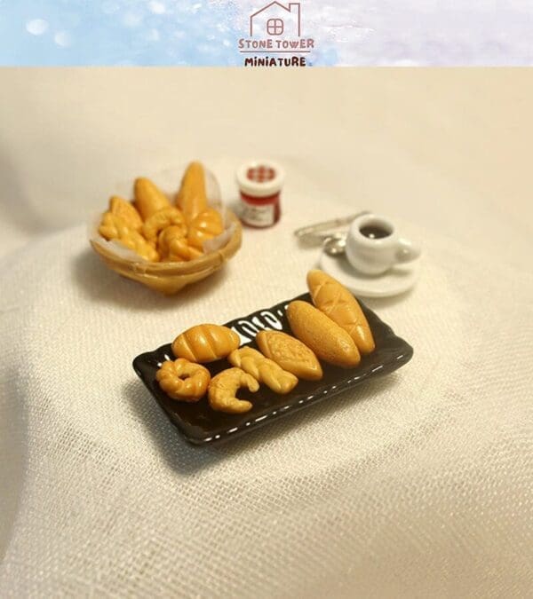 Miniature bread assortment on a black tray with coffee cup, spoon, and small jam jar on a white textured surface.