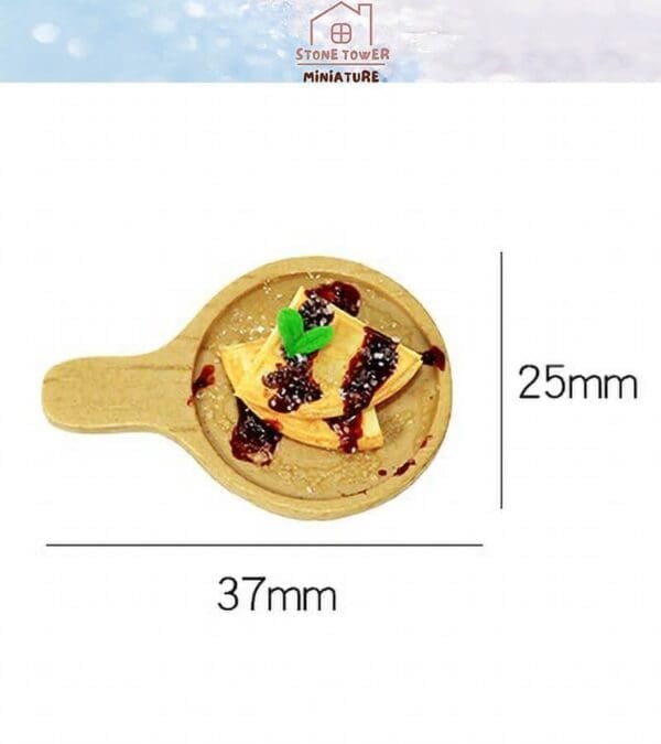 Miniature wooden pan with small pancakes, chocolate syrup, and mint leaf, measuring 25mm x 37mm.