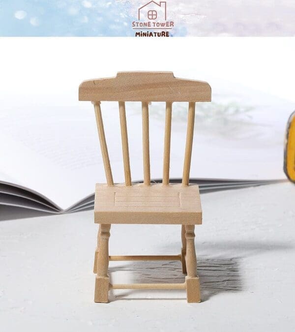 Wooden miniature chair model on a light surface with an open book in the background.