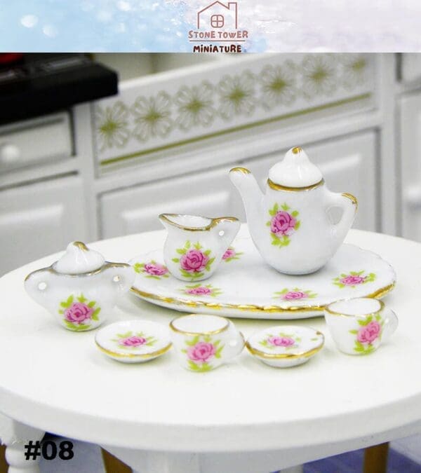 Miniature porcelain tea set with pink rose patterns, including teapot, creamer, sugar bowl, cups, and saucers on a white table.