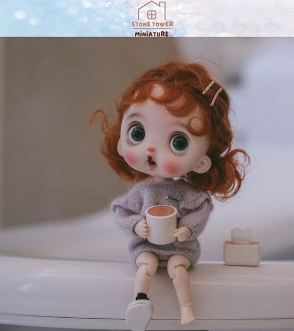 A doll with red hair and wide eyes holds a cup, sitting on a surface next to a small box.