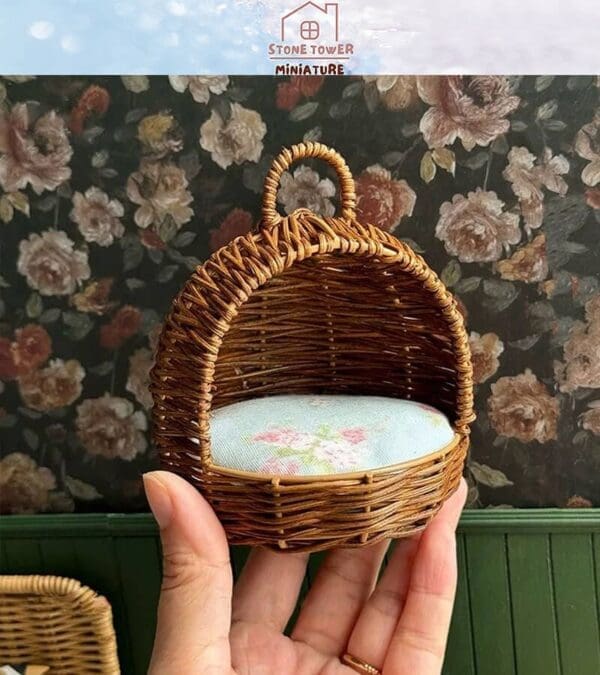 Hand holding a miniature wicker chair with a floral cushion, against a floral wallpaper background.