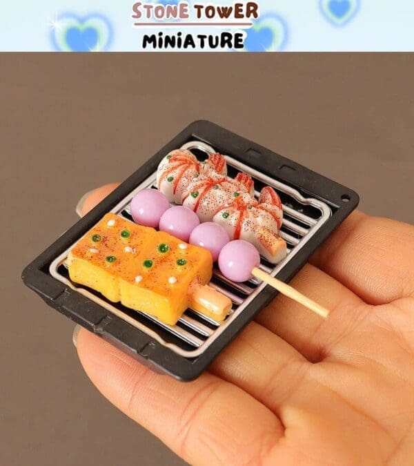 Miniature grilled skewers with shrimp, pink balls, and yellow squares on a tray held in a hand.