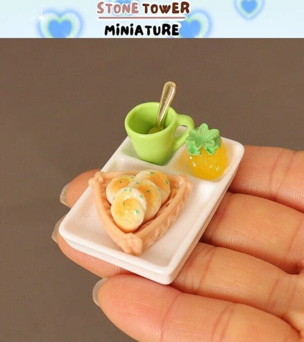 Miniature breakfast on a hand: waffles, banana slices, a green mug with spoon, and a pineapple slice on a tray.