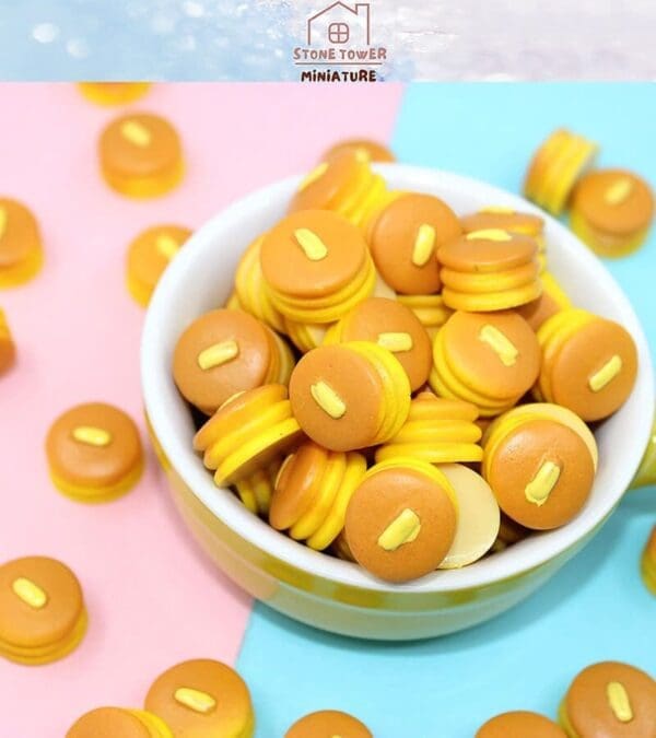 Miniature pancakes with butter, in a white bowl, on a colorful pink and blue background.