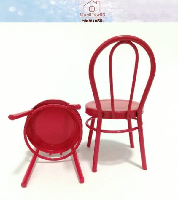 Two miniature red metal chairs, one upright and the other upside down, against a light background.