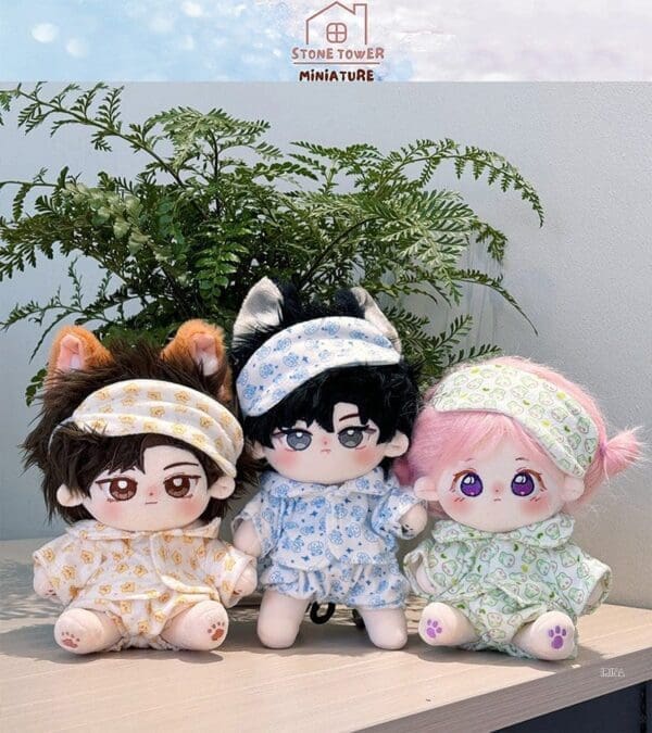 Three plush dolls with colorful pajamas and headbands sit in front of green foliage.