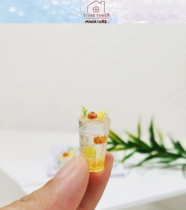 Fingers holding a tiny, detailed miniature drink with citrus slices and ice.