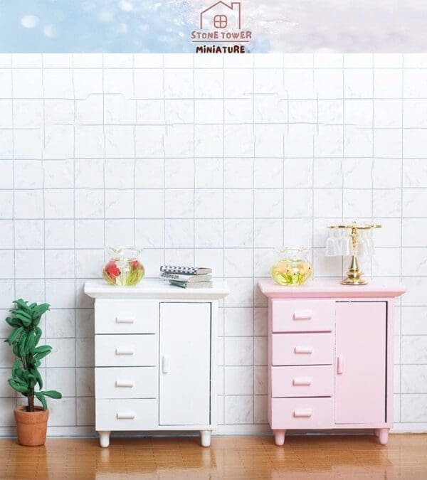 Two miniature cabinets, one white and one pink, with small decor items atop, set against a tiled wall background.