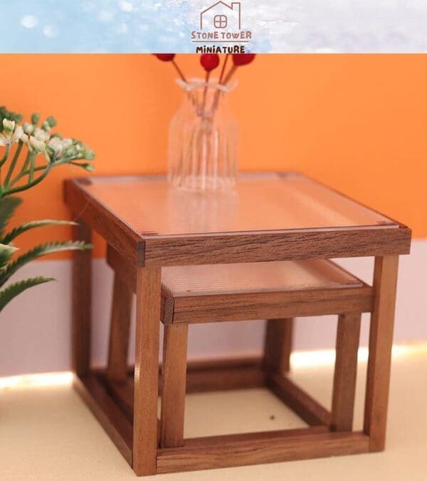 Miniature wooden nesting tables with a glass vase holding red flowers, set against an orange background.