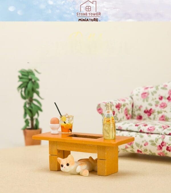 Miniature scene with a cat under a table, drinks on top, floral couch, plant in background, and Stone Tower Miniature logo.