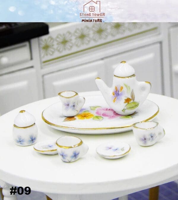 Miniature floral tea set with a tray, teapot, cups, saucers, and a sugar bowl on a white table.