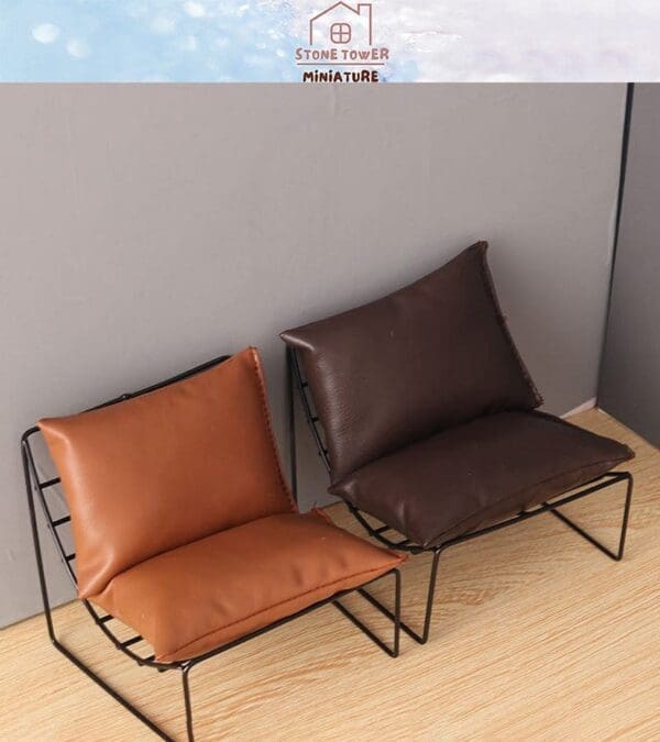 Two miniature leather lounge chairs, one brown and one dark brown, on a wooden floor against a gray wall.