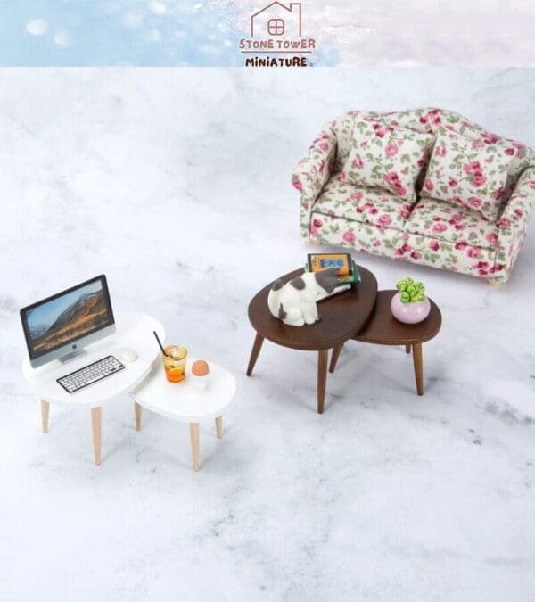 Miniature living room with floral couch, tables with laptop, orange drink, cat figurine, books, and plant on marble floor.