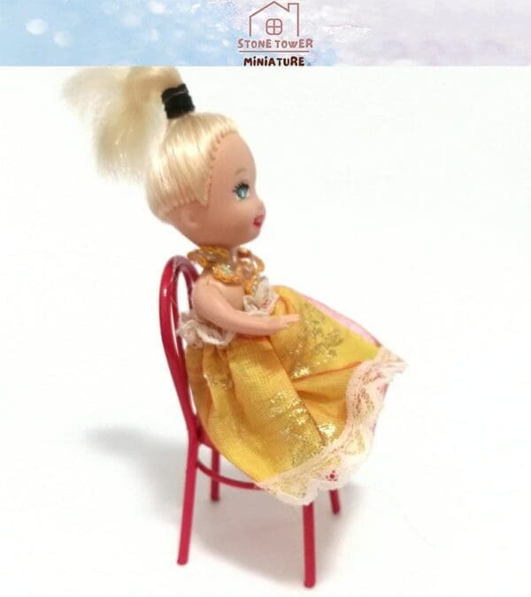 Blonde doll in a yellow dress, seated on a red chair with a white background.