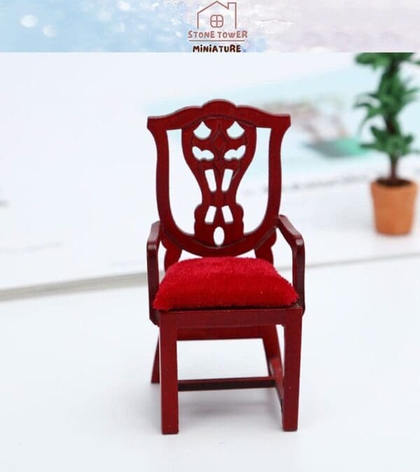 Miniature wooden chair with a red velvet cushion, intricate backrest design, placed on a white surface.