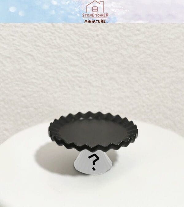 Black scalloped tray on a cone stand with a question mark, set against a white textured wall.