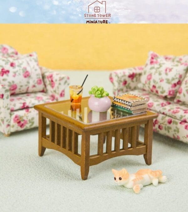 Miniature living room with floral sofas, wooden coffee table, drink, books, vase, and a small cat figurine on the floor.