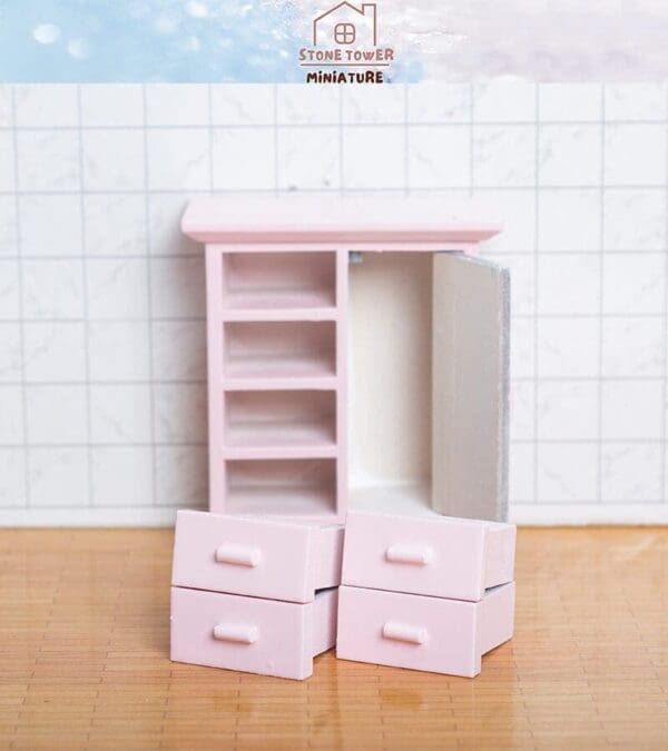 Miniature pink furniture set with open cabinets and drawers on a tiled and wooden surface.