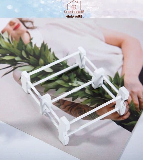 White miniature fence model placed on a photograph of a person holding a green leafy plant.