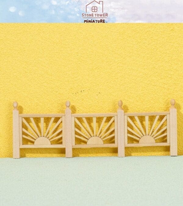 Miniature wooden fence with sunburst design against a textured yellow background and blue sky.