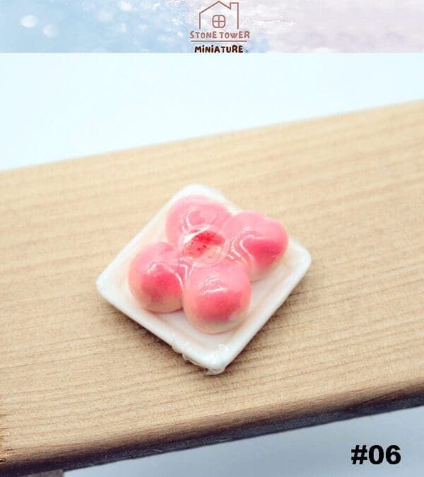 Pink miniature flower-shaped pastry on a small square plate, placed on a wooden surface.