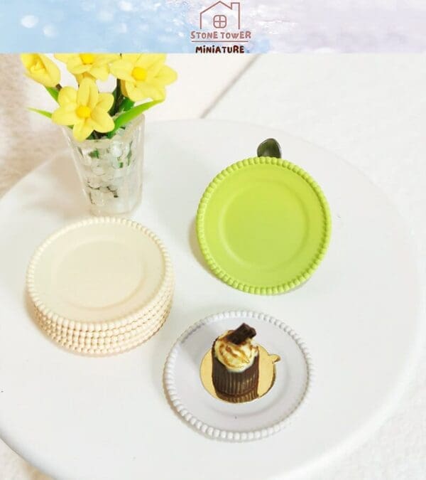 Miniature yellow flowers in vase, green and white plates, and a chocolate dessert on a white surface.