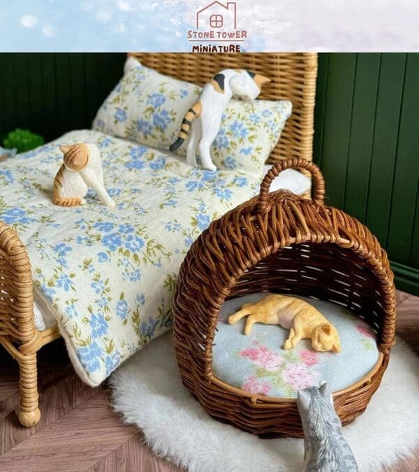 Miniature cats on a floral bedspread and in a wicker pet bed, with a toy cat looking on, creating a cozy scene.