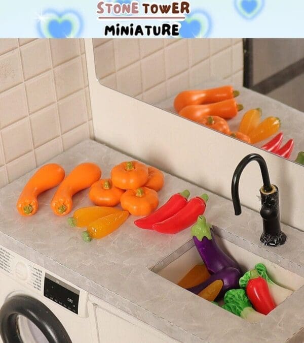 Miniature kitchen counter with assorted plastic vegetables, including peppers, carrots, and eggplants, near a tiny sink.