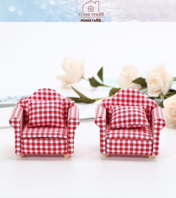 Two miniature red plaid armchairs with matching pillows on a white surface, with roses in the background.