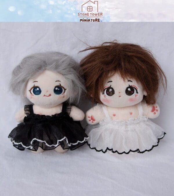 Two cute plush dolls in black and white dresses with expressive eyes, sitting on a white surface.