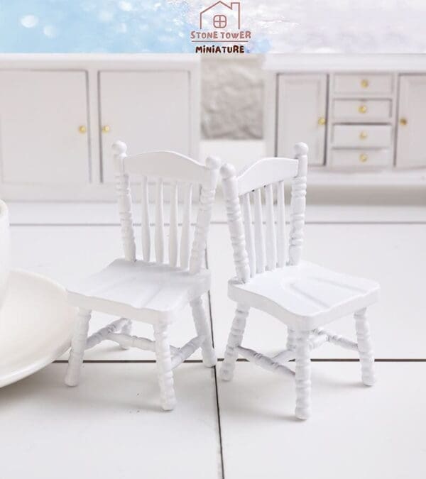 Two miniature white chairs on a white surface, with matching white cabinetry in the background.