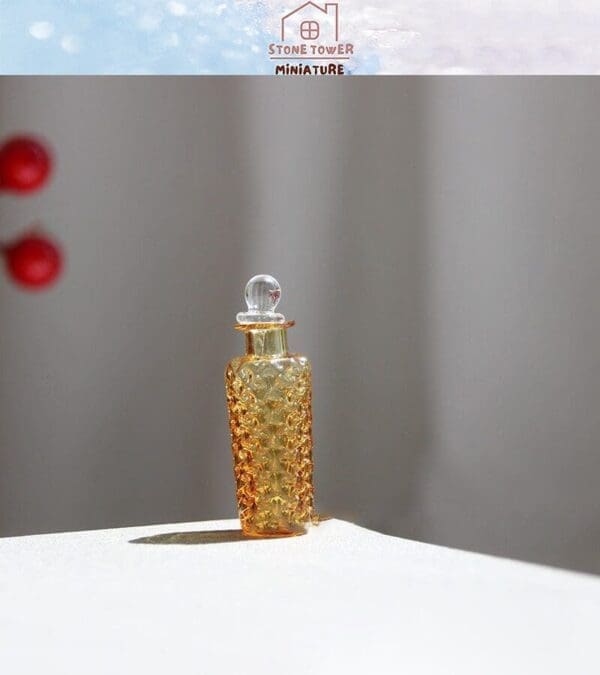 Miniature amber glass bottle with embossed pattern and round stopper, placed on a white surface with soft lighting.